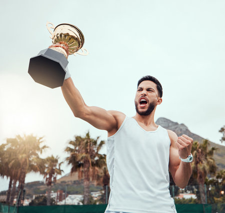 Mixed race tennis player holding trophy and celebrating success after winning court game. Hispanic fit athlete holding prize award and cheering in match. Active healthy man playing competitive sportの写真素材