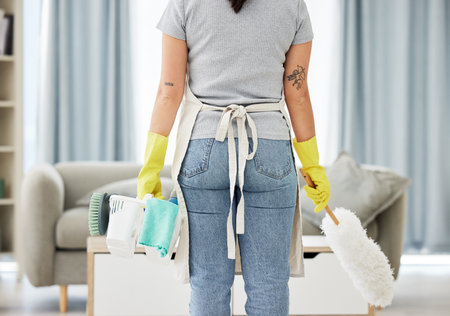 One unknown mixed race woman holding cleaning supplies while cleaning her apartment. An unrecognizable domestic cleaner wearing latex cleaning gloves with a collection of cleaning productsの写真素材