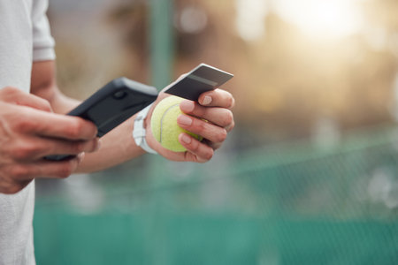Closeup of unknown mixed race tennis player using cellphone and credit card on court. Hispanic fit athlete paying for sports membership on a phone in club. Active healthy man buying renew subscriptioの写真素材
