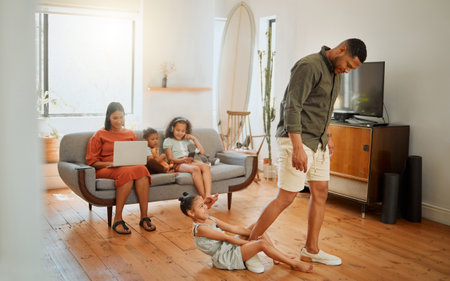 A mixed race family of five in the living room together. One African American father leaving while his daughter playfully clings to his legの写真素材
