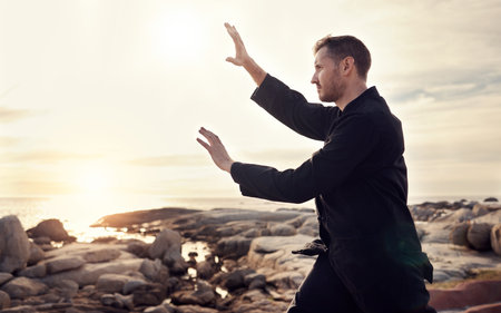 Nature, zen and tai chi, man on beach for balance and peace for mental wellness or control of body and mind. Spiritual health, fitness and meditation, energy and self care on rocks at sea in sunset.の写真素材