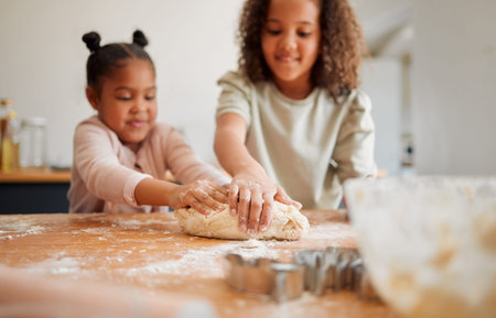 Two happy mixed race sisters having fun while baking together at home. Children only being playful...
