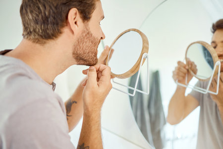 One handsome man checking his teeth in a bathroom at home. Caucasian male cleaning his teeth and looking in a mirror in his apartment.の写真素材