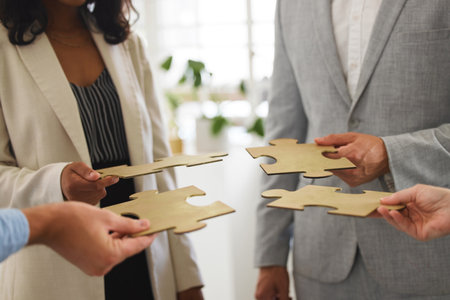 Group of businesspeople holding and fitting puzzle pieces together in an office at work. Business professionals solving a jigsaw problem in a meetingの写真素材