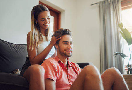 Loving young caucasian couple sitting together at home spending time and happy to be together. Happy young woman sitting on couch while her boyfriend sits between her legs as she plays with his hair.の写真素材