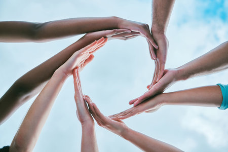 Closeup of diverse group of people from below joining hands together to form circle shape expressing...