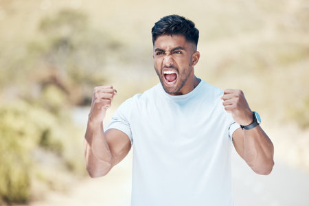 Closeup of a young mixed race man celebrating while out for a workout. Indian male looking ecstatic and cheering outside after a workout in natureの写真素材