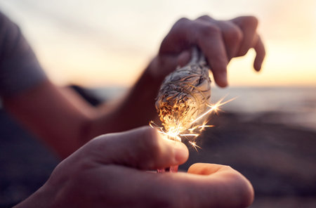 Hand, flame and sage burning at the beach for a spiritual ritual and meditation practice. Herb,...