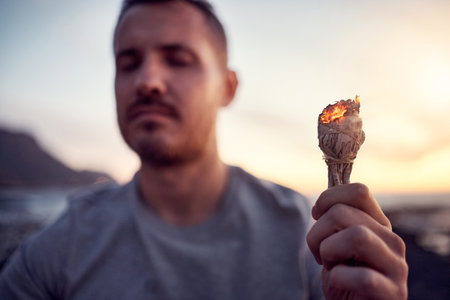 Man, hand and burning sage on the beach while meditating for spiritual peace and zen mindfulness. Herb, burn and alternative cleanse ceremony to meditate for smudge during a seaside peaceful timeの写真素材
