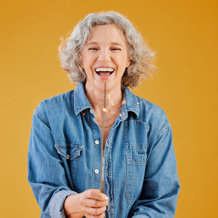 One happy mature caucasian woman playing with a sparkler on her birthday while posing against a...