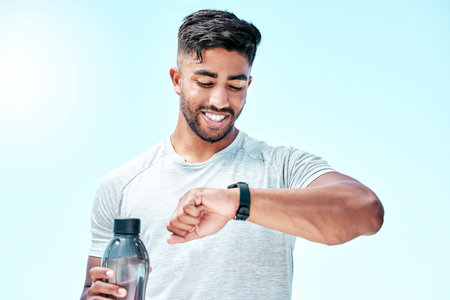 Athletic young mixed race man looking at his watch while exercising outdoors. Handsome hispanic male...