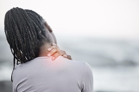 Black woman, neck and back pain on beach for fitness exercise, body wellness or sports training outdoor. African woman, body injury and shoulder muscle emergency or workout acciedent by ocean seaの写真素材