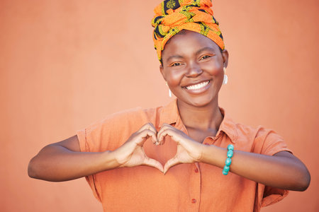 Black woman, hands or heart sign on wall background with fashion, trendy or stylish clothes for love, support or trust. Portrait, smile or happy student and hand gesture, hope emoji or orange mockupの写真素材