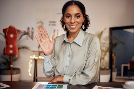 Wave, fashion and pallet with a black woman designer on a video call in her studio office at night. Portrait, waving and hand gesture with an employee at work for digital meeting in a design workshopの写真素材