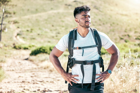 Athletic young mixed race man wearing a backpack taking a break during a hike. Fit handsome hispanic...