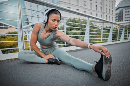 Young mixed race female athlete wearing headphones and listening to music while stretching before a...