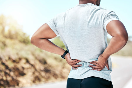 Closeup fit mixed race man holding his back in pain while exercising outdoors. Unrecognizable male...