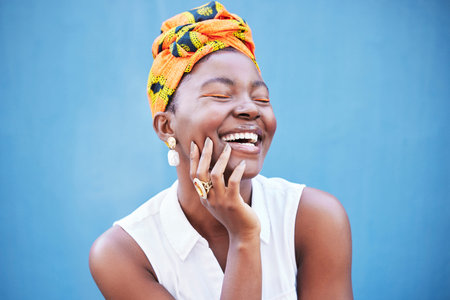 Happy black woman, african fashion and culture with turban scarf on blue wall background in Nigeria....