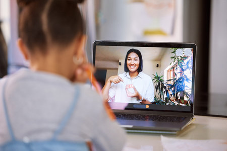 Little girl on a video call with her teacher using a laptop. Young female teacher doing a virtual...