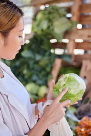 Grocery store, lettuce and Asian woman shopping and looking at vegetable quality and sale. Customer holding and checking vegetables price on salad promotion in a health food shop or supermarketの写真素材