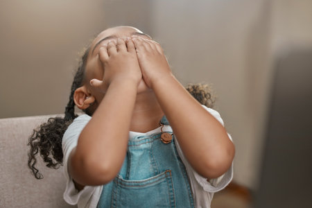 Child, hands on face and covering eyes for hide and seek game at home while playing for fun, entertainment and fun activity. Cute girl kid on house chair while hiding, playful and doing peekabooの写真素材