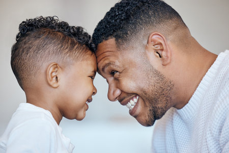 Cute little boy and dad touching foreheads. Closeup of happy dad and son looking into each others eyes. African american family expressing love and support, enjoying tender moment together at homeの写真素材