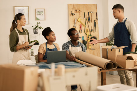 Creative leader, manager or boss talking to his design team in a modern studio or workshop. Male designer speaking to a group of colleagues and coworkers in a tailor, textile or fashion outfitterの写真素材