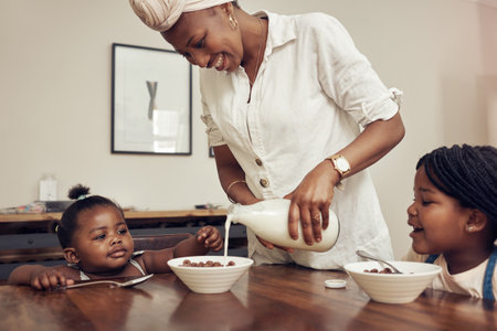 No one loves cereal more than they do. a young mother preparing cereal for her two adorable young daughters at home.の写真素材