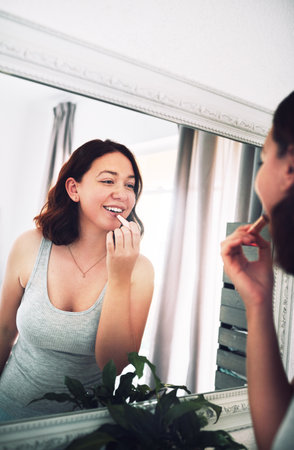 I really picked the perfect colour for my lips. an attractive young woman applying lipstick while standing in front of the mirror in her bedroom at home.の写真素材