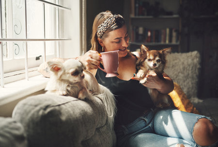 Its not a home with dogs. a young woman having coffee and relaxing with her dogs on the sofa at home.の写真素材
