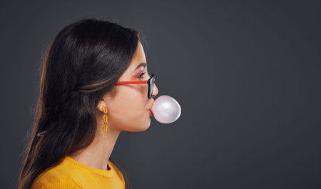 Blowing bubbles. an attractive teenage girl standing against a dark background alone and blowing...