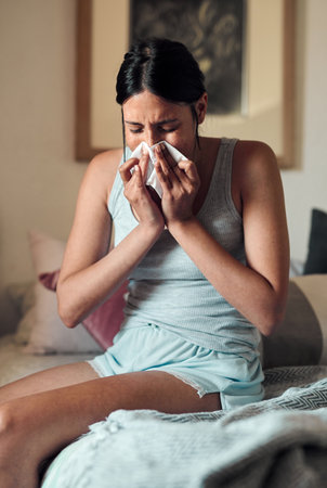 No, not the flu...a young woman blowing her nose with a tissue at home.の写真素材