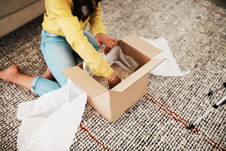 Who doesnt love surprises. an unrecognizable businesswoman sitting alone on her living room floor and opening up a mystery box.の写真素材
