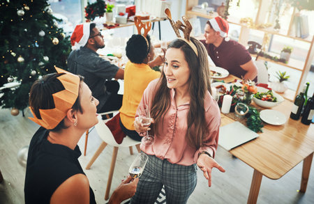 Christmas time can be a great time to catch up. High angle shot of two attractive female friends having a chat with their friends dining for Christmas in the background.の写真素材