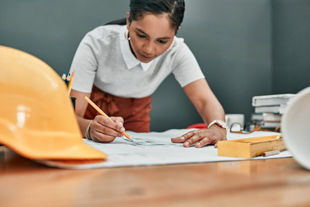 Putting her mind to a new design. a young architect working with blueprints in an office.の写真素材