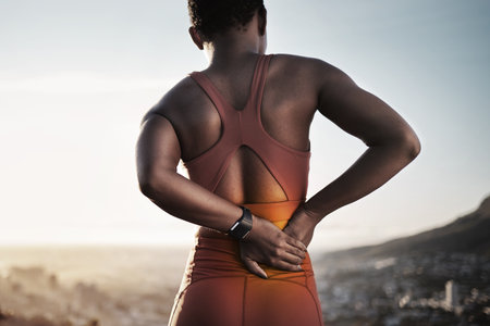 Back pain, fitness and black woman with spine injury from outdoor sports training. Athlete with backache, joint pain and stress on body muscle from exercise, running and first aid health emergencyの写真素材