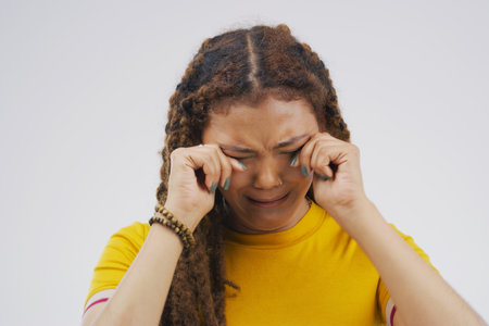 This sucks. Studio shot of a young woman crying while standing against a gray background.の写真素材