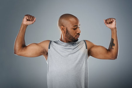 Im strong and thats enough. a sporty young man flexing his muscles against a grey background.の写真素材