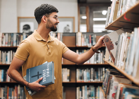 University, student or man with bible in a library to study spiritual religion knowledge, prayer or...