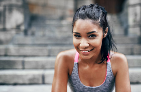 Shes in the mood to burn some calories. Portrait of an attractive young sportswoman sitting down on a stairway outdoors in the city.の写真素材