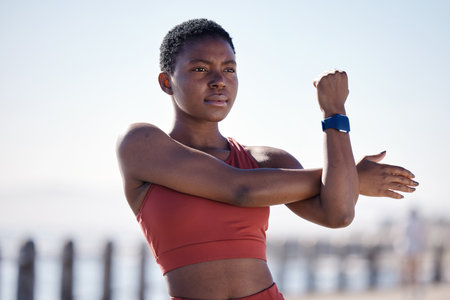 Fitness, exercise and black woman stretching in city for healthy lifestyle, wellness and cardio workout. Sports, motivation and female athlete ready to start running, marathon training and jog by seaの写真素材