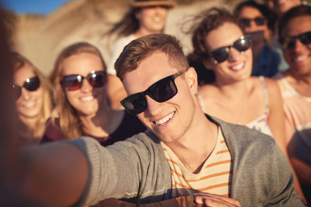 Take a selfie and let the good times roll. Cropped portrait of a handsome young man taking a selfie with his friends at the beach.の写真素材