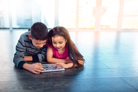 We dont get along all the time. two young children using a digital tablet while lying down on the...