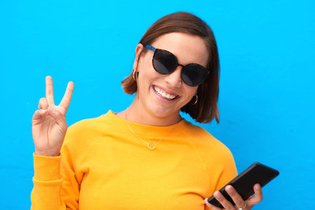 Peace out folks. Cropped portrait of a happy young woman showing the peace sign against a blue...