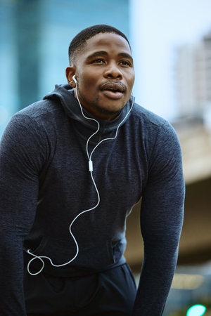 Breathe, black man and fitness break for city workout, wellness exercise and running outdoors. Runner, breathing and relax after cardio marathon with music earphones for motivation, mindset and goalsの写真素材