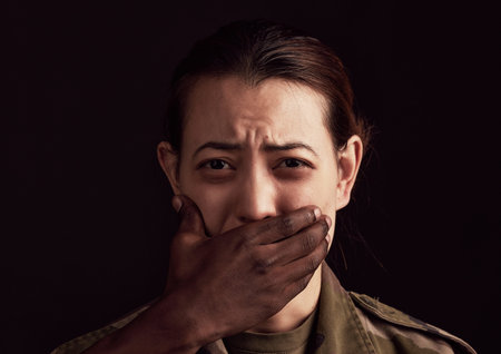 Abuse, fear and hand over the mouth of a woman in studio on a dark background to stop gender...