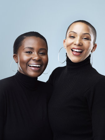 Polo necks suit us we know. Portrait of two beautiful young women holding each other while standing against a grey background.の写真素材