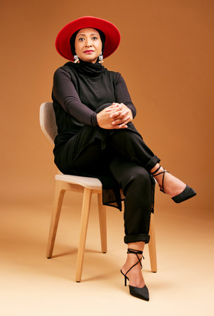 Muslim woman, studio background chair or fashion hat in luxury style, trend or classy clothes with empowerment or self love mindset. Portrait, confident or mature islamic model in designer clothingの写真素材
