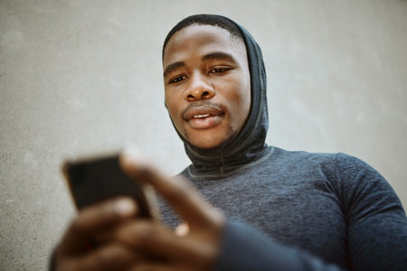 Fitness, black man and phone typing in city to check social media, internet or search mobile app, online sports blog and exercise tech. Young athlete reading notification on smartphone before workoutの写真素材