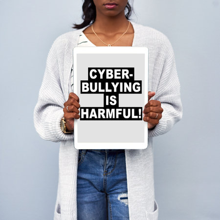 Studio shot of an unrecognizable young woman holding a tablet with the message CYBERBULLYING IS HARMFUL on the screen against a grey backgroundの写真素材